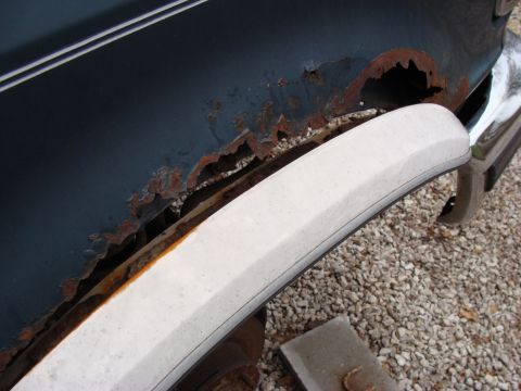 1993 Ford Bronco - Severe rust is visible on the wheel well of this dark blue vehicle, with a white trim piece obscuring part of the damage.