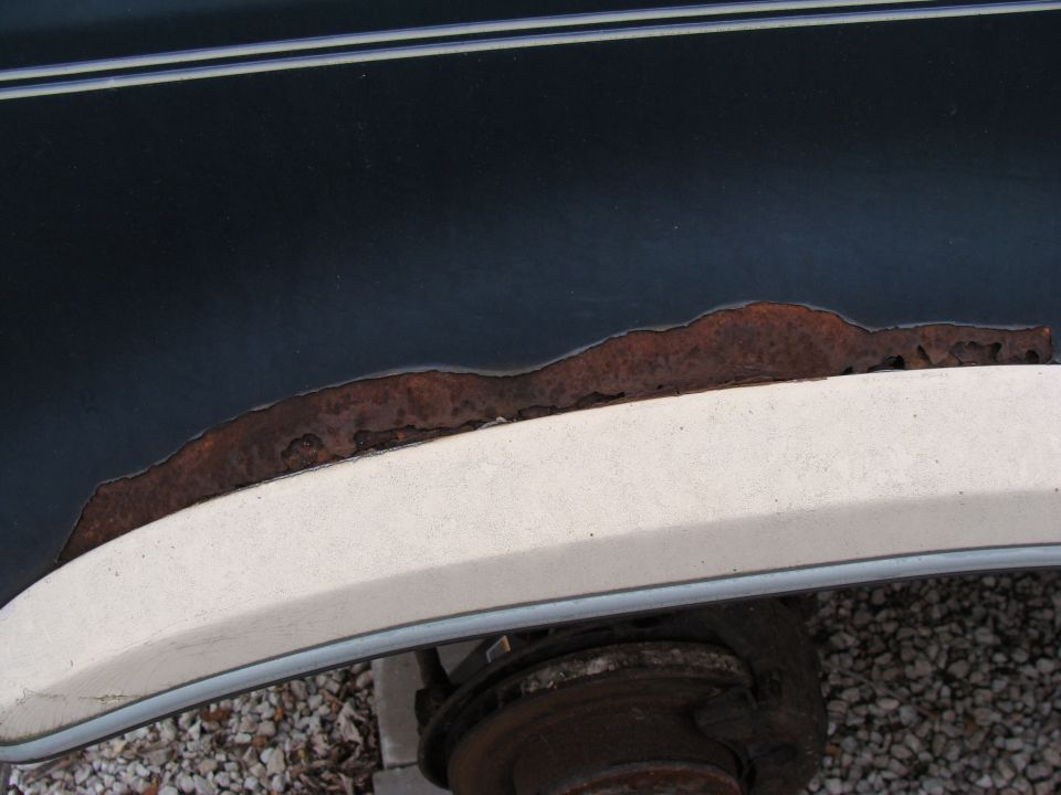 Dark blue vehicle's rear wheel well with significant rust damage and a white trim piece