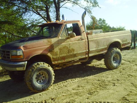 1990 Ford Bronco - This heavily modified pickup truck, likely a 1992 Ford F-Series, is covered in mud and features a prominent exhaust stack.