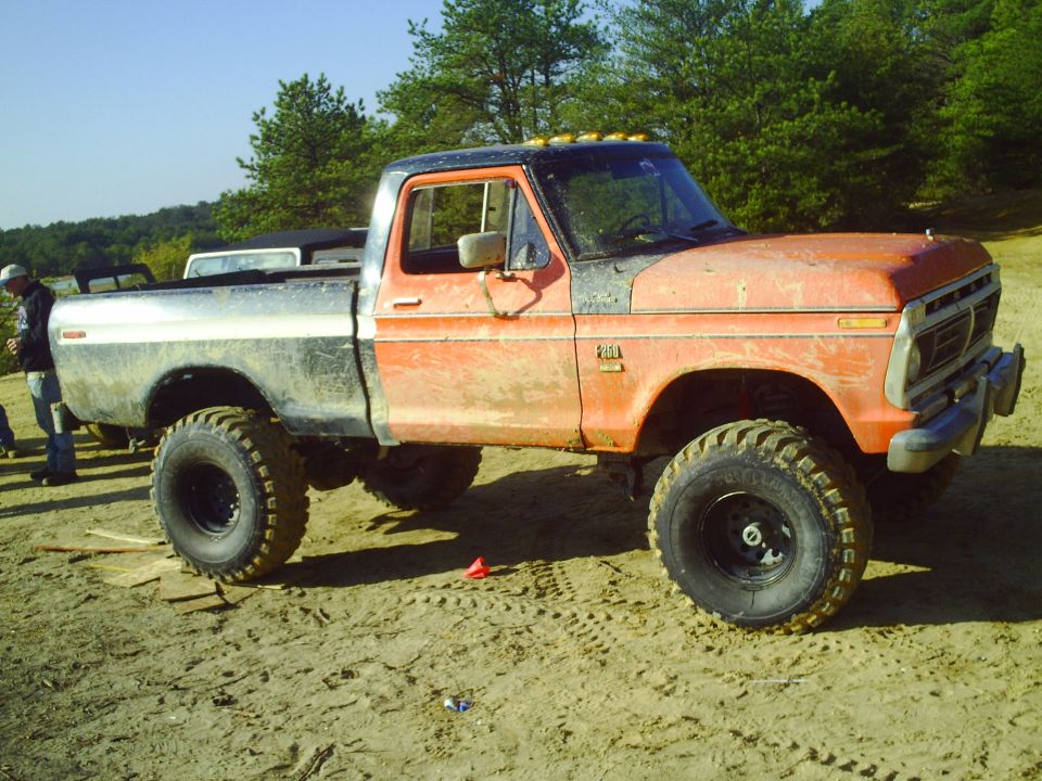 Orange and silver lifted pickup truck with large off-road tires parked on sandy ground