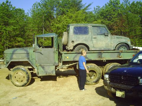 1990 Ford Bronco - A flatbed truck carries a small SUV, with a person standing nearby and another vehicle partially visible.