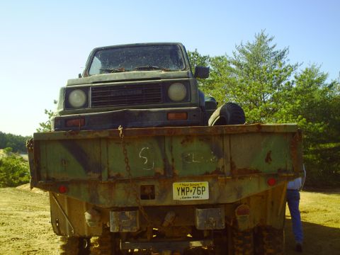 1990 Ford Bronco - A Suzuki Samurai is loaded onto a weathered flatbed truck, viewed from the rear.