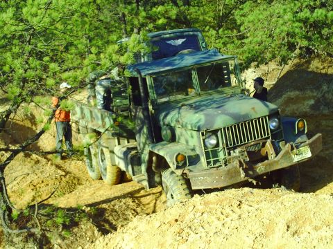 1990 Ford Bronco - Military truck navigating rough terrain with assistance from another vehicle.