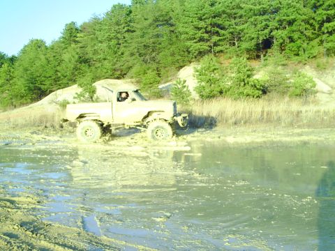 1990 Ford Bronco - A lifted pickup truck navigates through a muddy, waterlogged terrain.