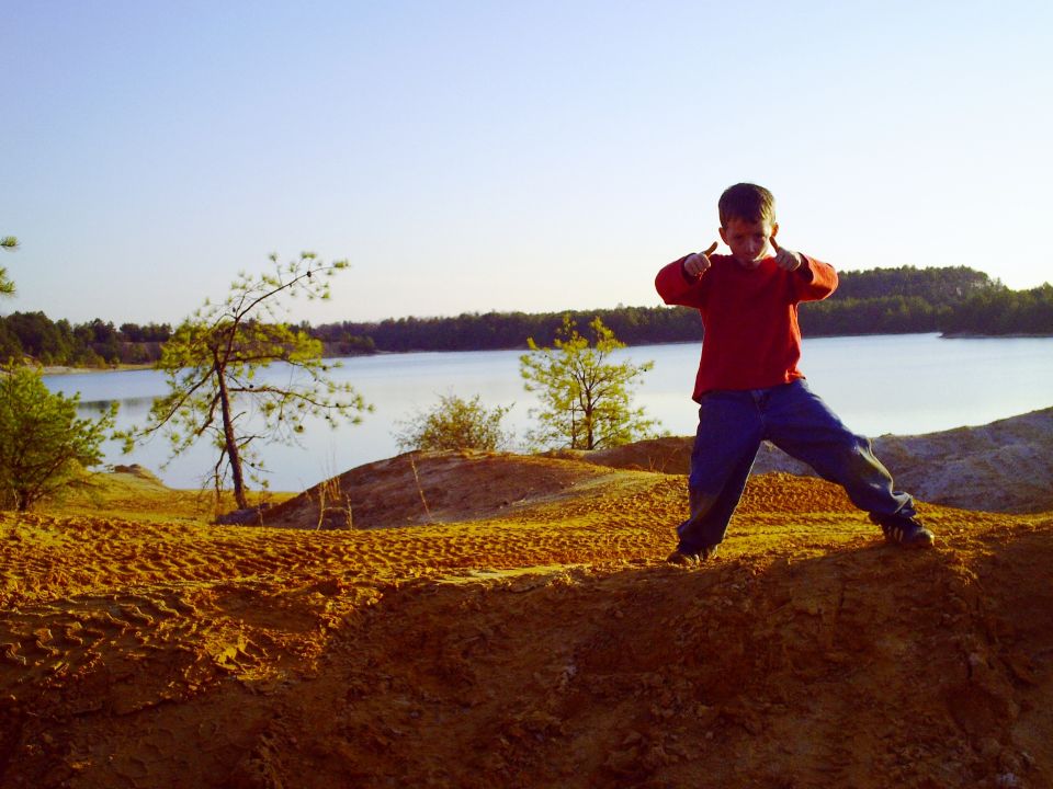 Child giving thumbs up on a sandy hill overlooking a lake