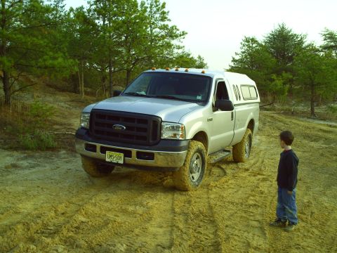 1990 Ford Bronco - Silver Ford F-250 Super Duty truck with camper shell on a dirt path, a boy watches.