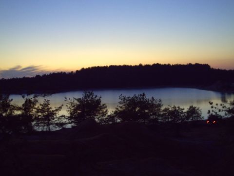 1990 Ford Bronco - A tranquil lake scene at twilight, with the silhouette of trees against a fading sky and distant vehicle lights.