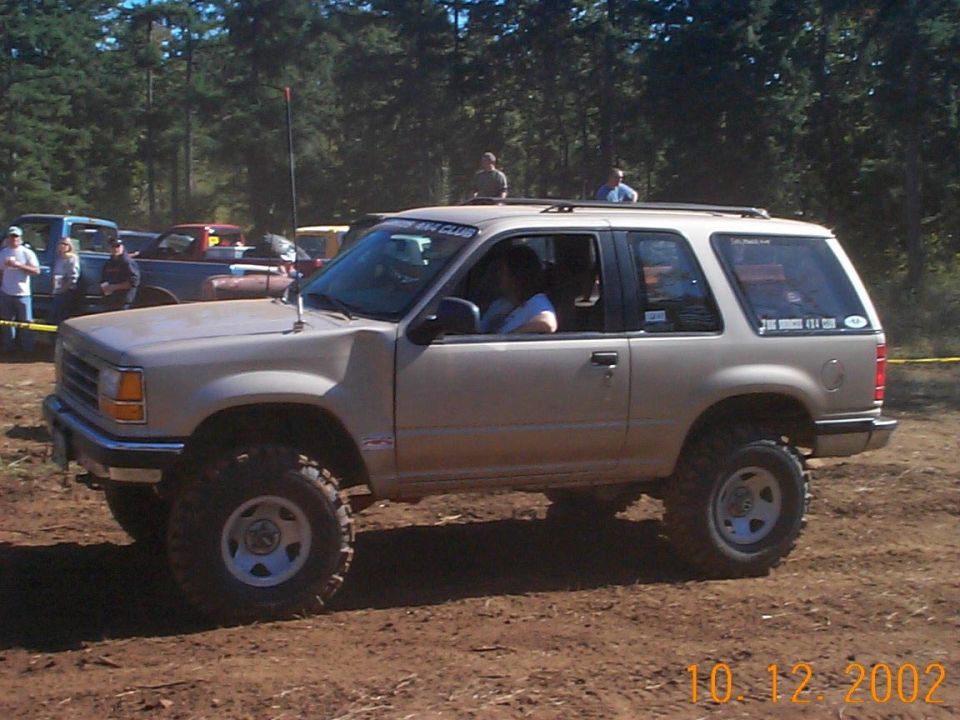 Tan lifted two-door Ford Explorer on large tires, side view at dirt off-road event