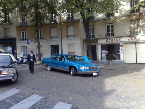 1991 Ford Crown Victoria - A blue Cadillac limousine is parked on a cobblestone street in front of a garage.
