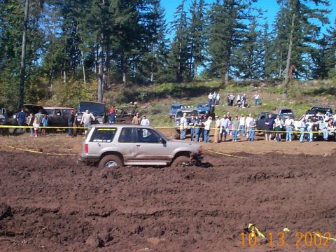 1994 Ford Explorer - A 1994 Ford Explorer navigates a challenging mud pit at an off-road event, with spectators watching from the sidelines.