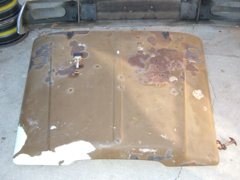 1988 Ford Bronco - Removed truck hood laid face-up on a concrete driveway, painted tan-brown with large patches of surface rust, bare metal and old white pain…