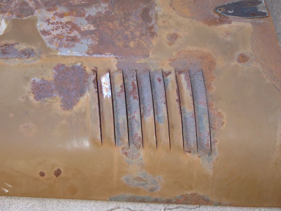 Close-up of rusty stamped louver vents in a tan painted sheetmetal hood panel