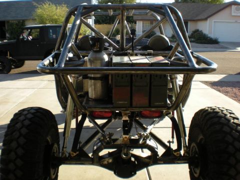 Suzuki Samurai - Straight-on rear view of a bare-steel tube-chassis rock buggy on a driveway, with three olive-drab military ammo cans and a polished air/CO…