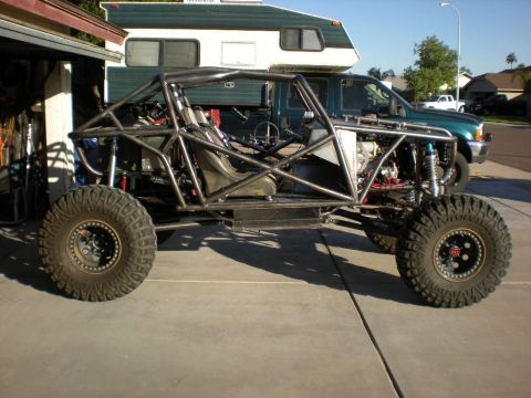 Suzuki Samurai - A bare tube-chassis rock buggy shown in side profile, with a bare metal roll cage, two racing seats, coilover shocks, and large mud-terrain…