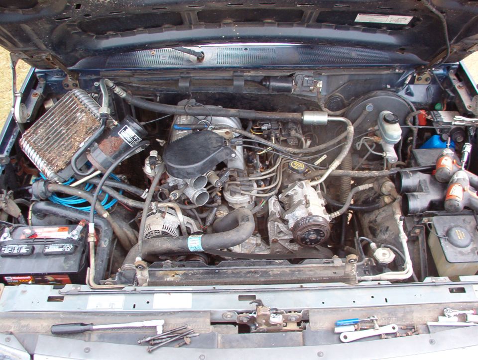 Engine bay of older Ford pickup or SUV with inline engine, alternator and battery visible