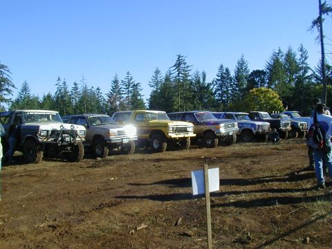 1994 Ford Explorer - Multiple off-road vehicles are parked in a dirt lot under a clear blue sky.