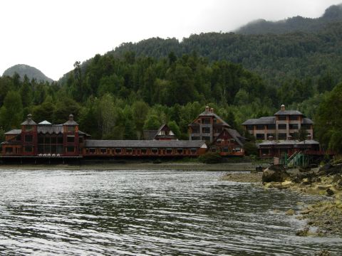 1986 Ford Bronco - Several large wooden structures are situated along the waterfront, backed by a dense forest and misty mountains.