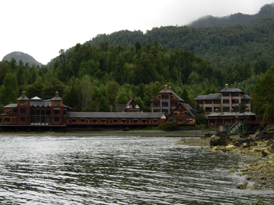 Large wooden buildings on the shore of a lake, with a forested mountain in the background