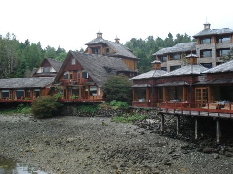 1986 Ford Bronco - A collection of wooden buildings with balconies and large roofs are situated on a rocky shore, with trees in the background.