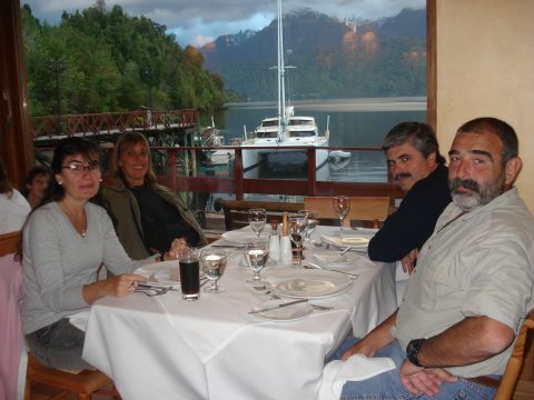 1986 Ford Bronco - A group enjoys a meal at a restaurant overlooking a lake with a large catamaran docked nearby and mountains in the distance.