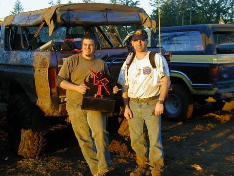 1994 Ford Explorer - Two men pose with a trophy after an off-road event, with their modified vehicles in the background.