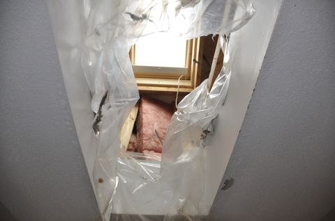 1996 Ford Bronco - A damaged ceiling reveals exposed insulation and wooden beams through torn plastic sheeting.