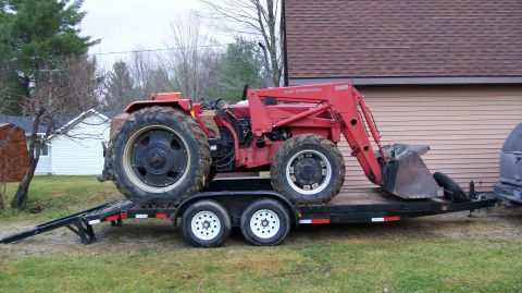 2000 Chevrolet Tahoe - A red tractor is being transported on a trailer, parked in a grassy area next to a building.