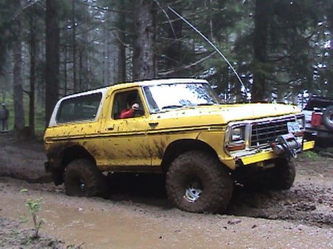 1994 Ford Explorer - A yellow 1978 Ford Bronco navigates a muddy off-road trail, with another vehicle visible in the background.