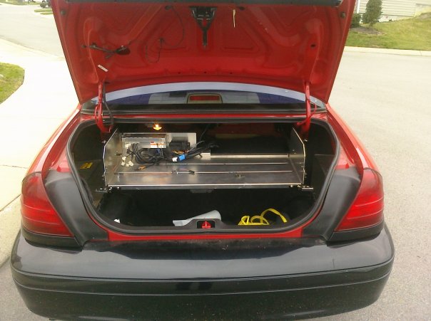 Rear of red car with trunk open, metal shelf with electronics inside