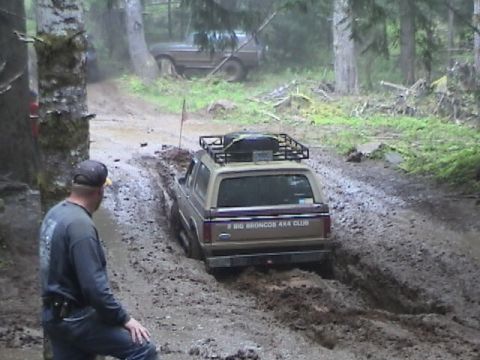 1994 Ford Explorer - Two Ford Broncos navigate a muddy trail through a forest.