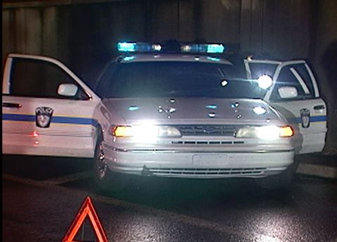 1997 Ford Crown Victoria - Two white 1997 Ford Crown Victoria police cars are parked with their doors open and emergency lights flashing.