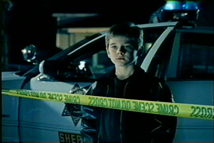 Police car behind crime scene tape with a boy in foreground