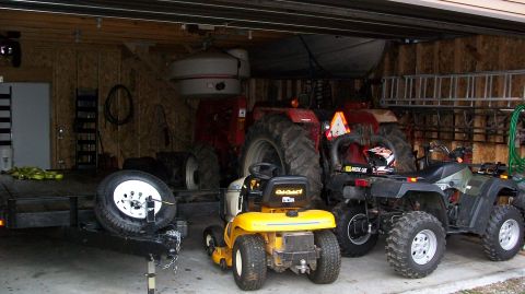 2000 Chevrolet Tahoe - A collection of vehicles including a trailer, riding mower, tractor, and ATVs are parked inside a garage.