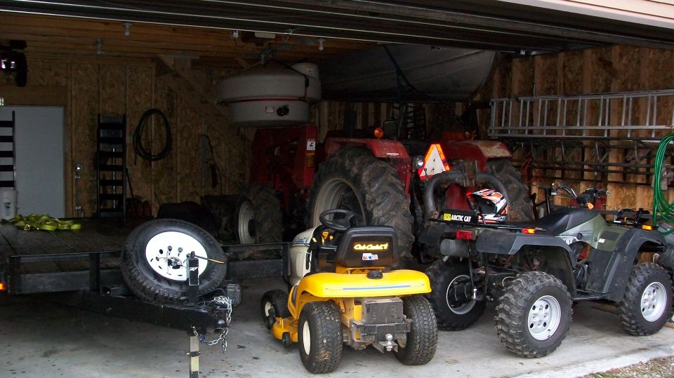 Garage scene with a trailer, yellow riding mower, red tractor, and two ATVs