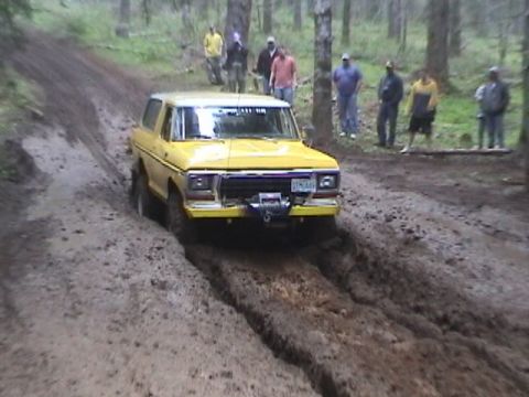 1994 Ford Explorer - A yellow Ford Bronco drives through a muddy trail in a wooded area with spectators watching.