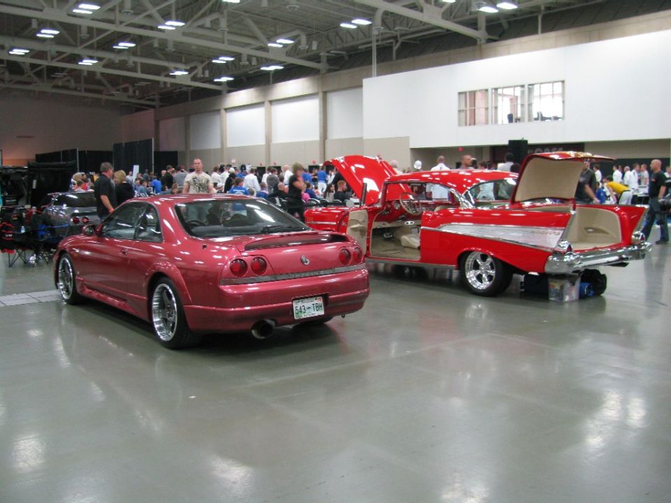 red coupe and red classic car with hoods and doors open inside a building