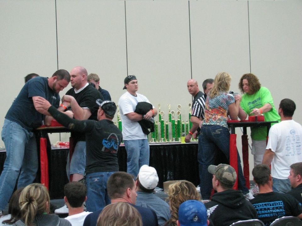 People arm wrestling at a competition with trophies on display