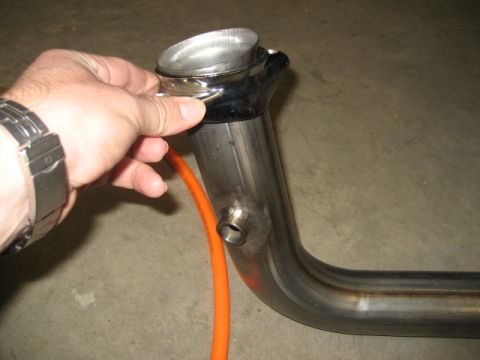1996 Ford Bronco - A person holds a chrome exhaust pipe fitting, with an orange hose connected to it.