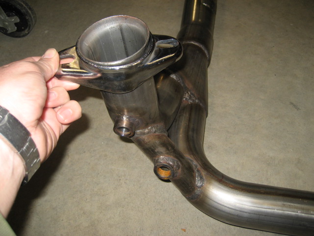 Exhaust pipe with a flange and two threaded ports, held by a hand with a watch