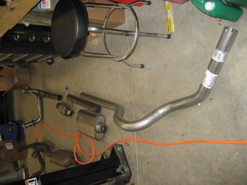 1996 Ford Bronco - Various exhaust system parts are laid out on a concrete floor, possibly for installation or repair.