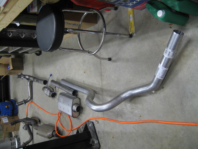 Exhaust system pipes and muffler laid out on a concrete floor