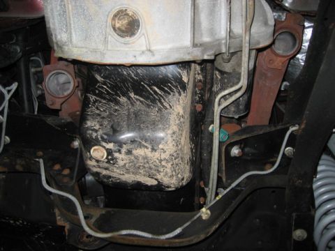 1996 Ford Bronco - Close-up view of the underside of a vehicle, focusing on the oil pan and exhaust components, showing signs of dirt and wear.