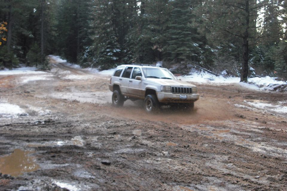 White Jeep Grand Cherokee driving through mud and snow on a wooded trail