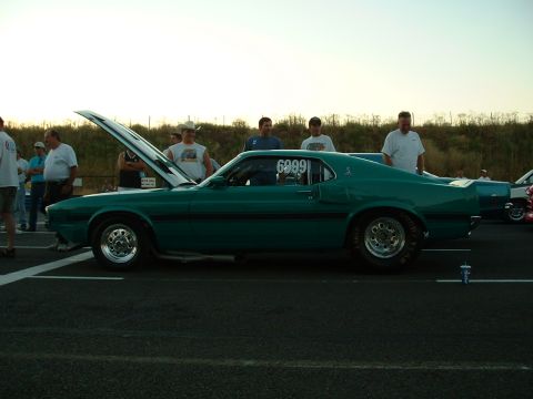 1991 Ford Bronco - A teal 1969 Ford Mustang Mach 1 is parked at a race track with its hood up and a race number on the door.