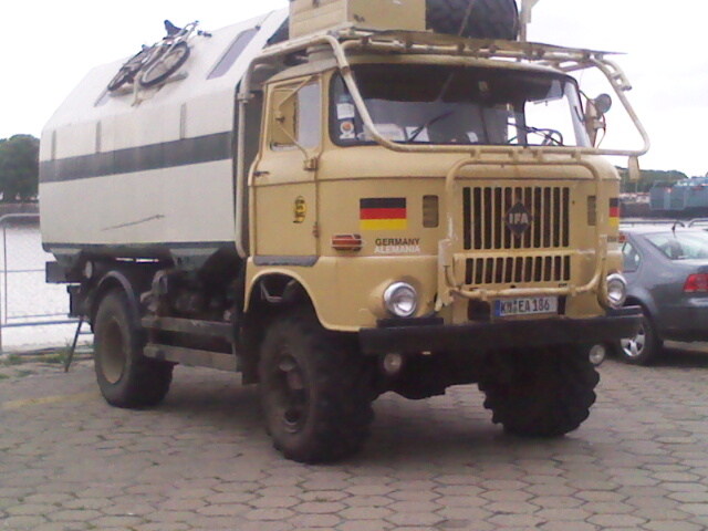 Tan IFA W50 4x4 expedition camper truck with German flag decals, front three-quarter view