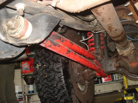1986 Ford Bronco - Close-up of the undercarriage shows suspension parts and a driveshaft, with some oil containers visible in the background.