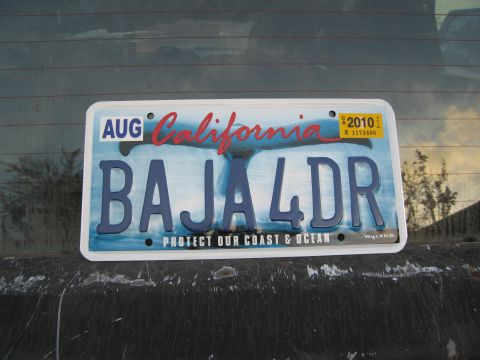 1986 Ford Bronco - California license plate with 'BAJA 4DR' and 'Protect Our Coast & Ocean' text.