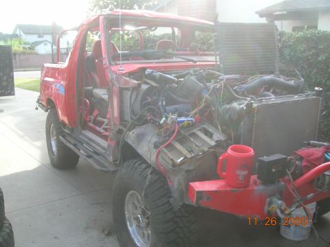 1985 Ford Bronco - This red SUV is undergoing extensive repairs, with its front end completely dismantled and the engine exposed.