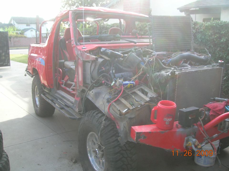Red SUV with front end disassembled, engine exposed, and custom roll cage visible