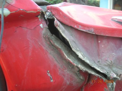 1985 Ford Bronco - Close-up of severely damaged red vehicle bodywork, showing bent metal and exposed filler material.